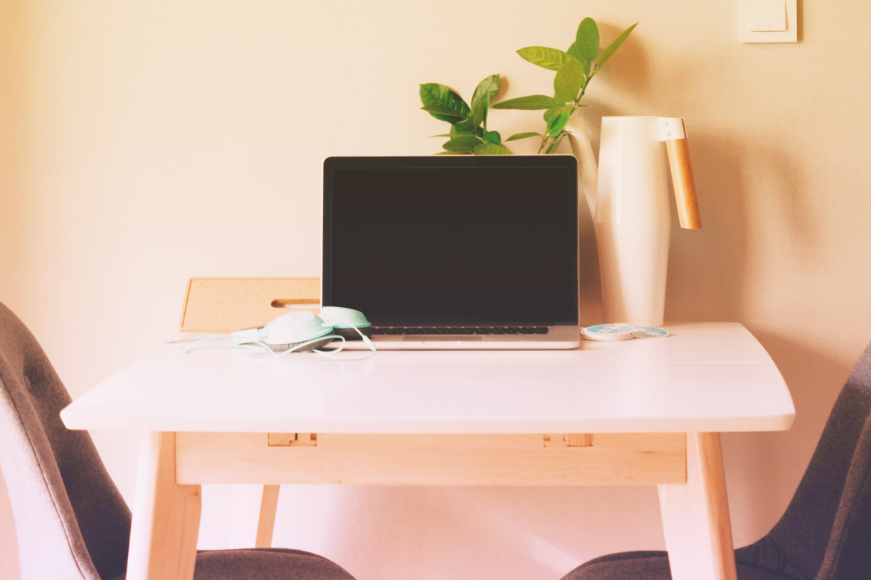 Small desk with laptop, mouse, plant and water bottle.