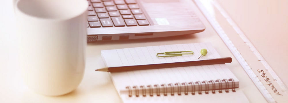 Closeup photo of part of a laptop, pen, paperclip and notebook.