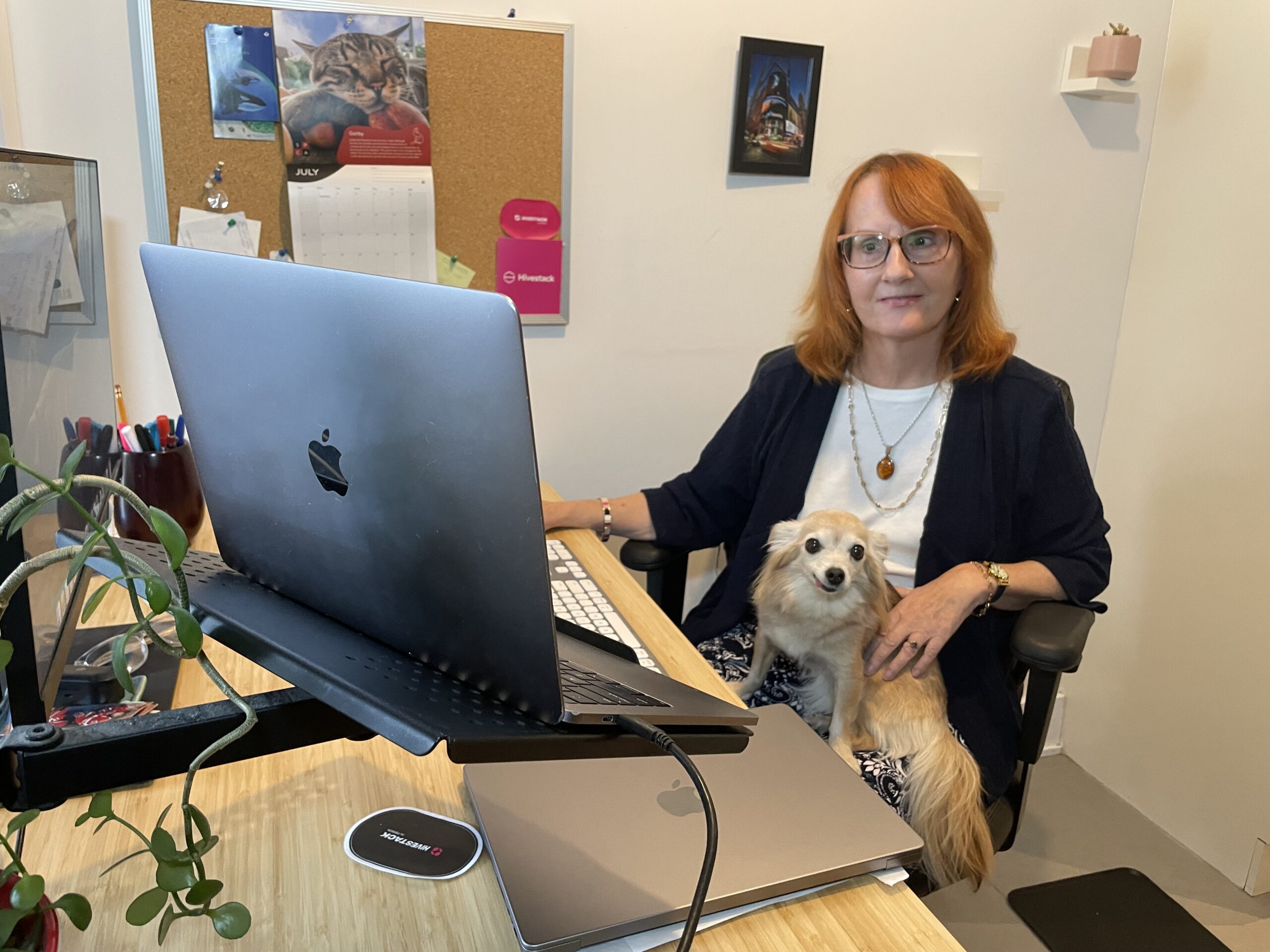 Catherine MacLaine sitting behind her computer in the office with her small dog on her lap